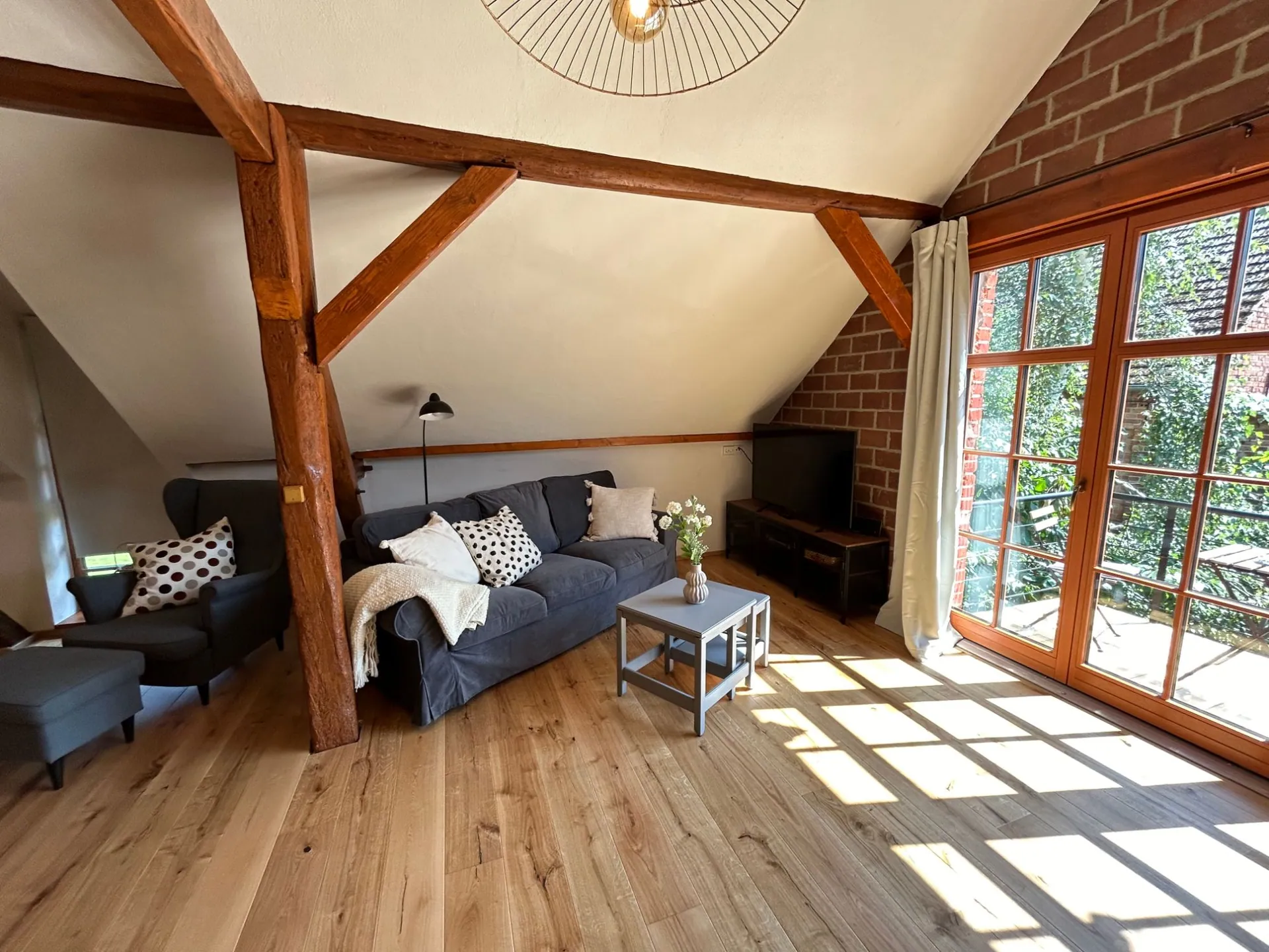 Ferienwohnung III: Wohnstube unter offenem Dachstuhl mit Sofa, Ohrensessel und Balkontür